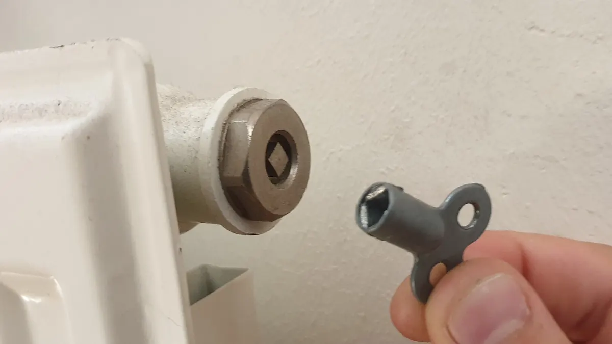Mano sujetando la llave de purga junto al purgador de un radiador blanco de agua