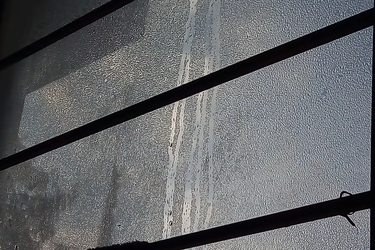 Cristal de ventana empañado por la condensación con gotas que resbalan hacia el marco